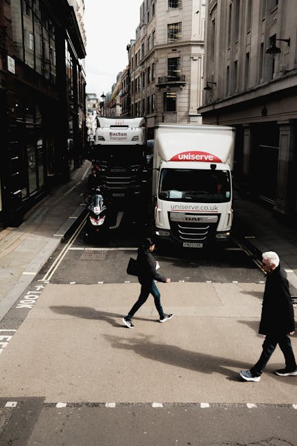Image depicting a narrow residential street in Ealing with a white van parked on the cobblestone road, which is lined with various potted plants and small trees outside terraced houses. The houses hav